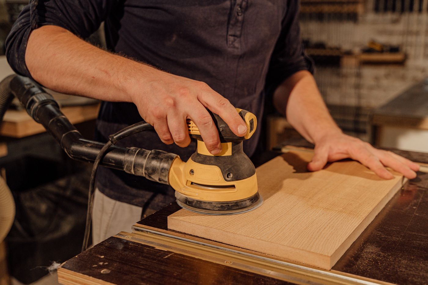 Handwerker schleift ein Holzbrett mit einem Exzenterschleifer mit angeschlossener Absaugung
