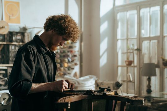 Handwerker restauriert ein antikes Moebelstueck in einer hellen Werkstatt